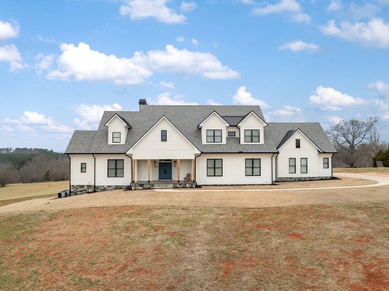 White board and batten home with a shingle roof on open land