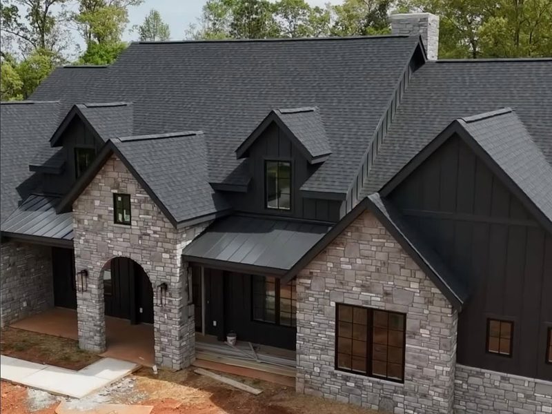 Dark board and batten home with stone and a metal porch roof